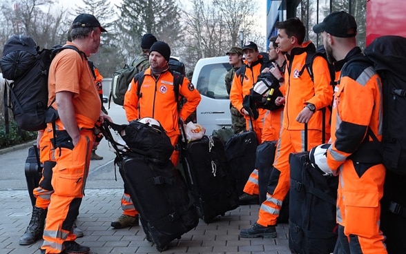 Zehn Personen, teils in orangen Kleidern, teils in Armeeuniform, stehen in einer Gruppe zusammen.