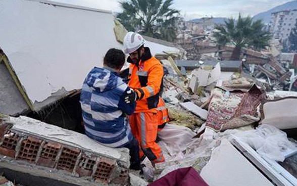 Ein Mitglied der Rettungskette spricht mit einer Person auf den Trümmern eines eingestürzten Hauses.