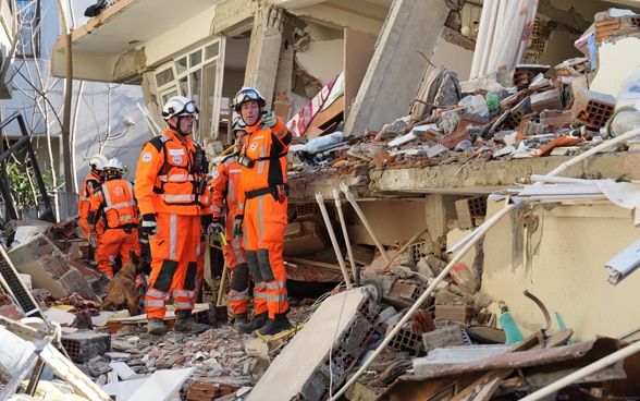 Zwei Mitglieder der Rettungskette stehen vor einem Gebäude, dessen Aussenwand zerstört ist.