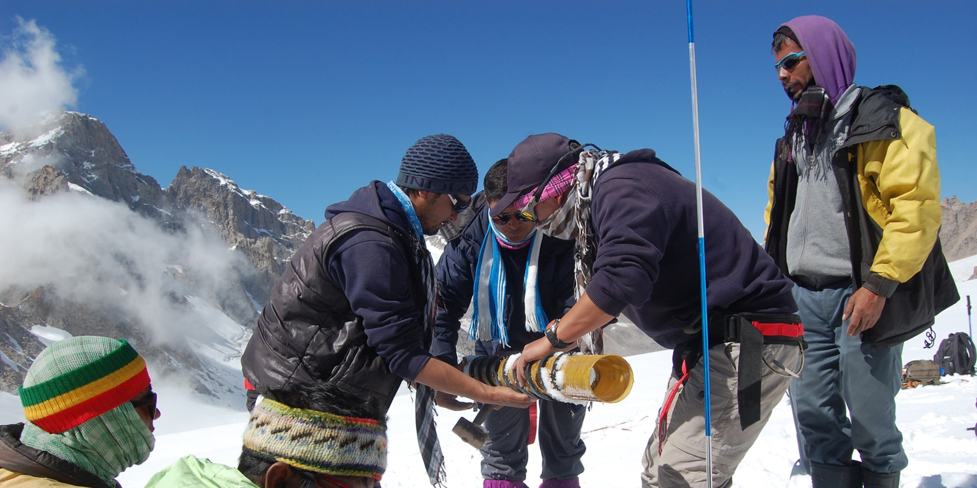 Sieben Männer führen auf einem Gletscher wissenschaftliche Messungen im Schnee durch. 