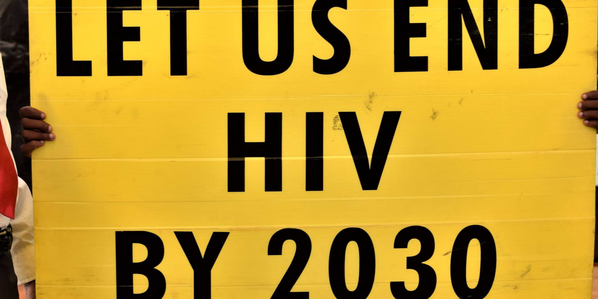 Ein junger Mann hält ein gelbes Plakat in die Luft auf welchem steht: «Wir wollen HIV bis 2030 besiegen.»