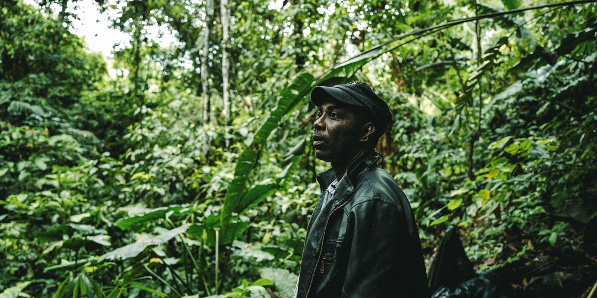 Un homme vêtu d’une veste en cuir, debout dans une jungle verte et luxuriante.