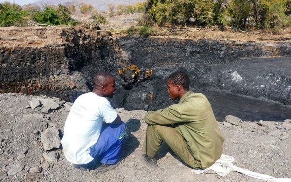 Two men sit and talk on the edge of a crater in Zimbabwe.