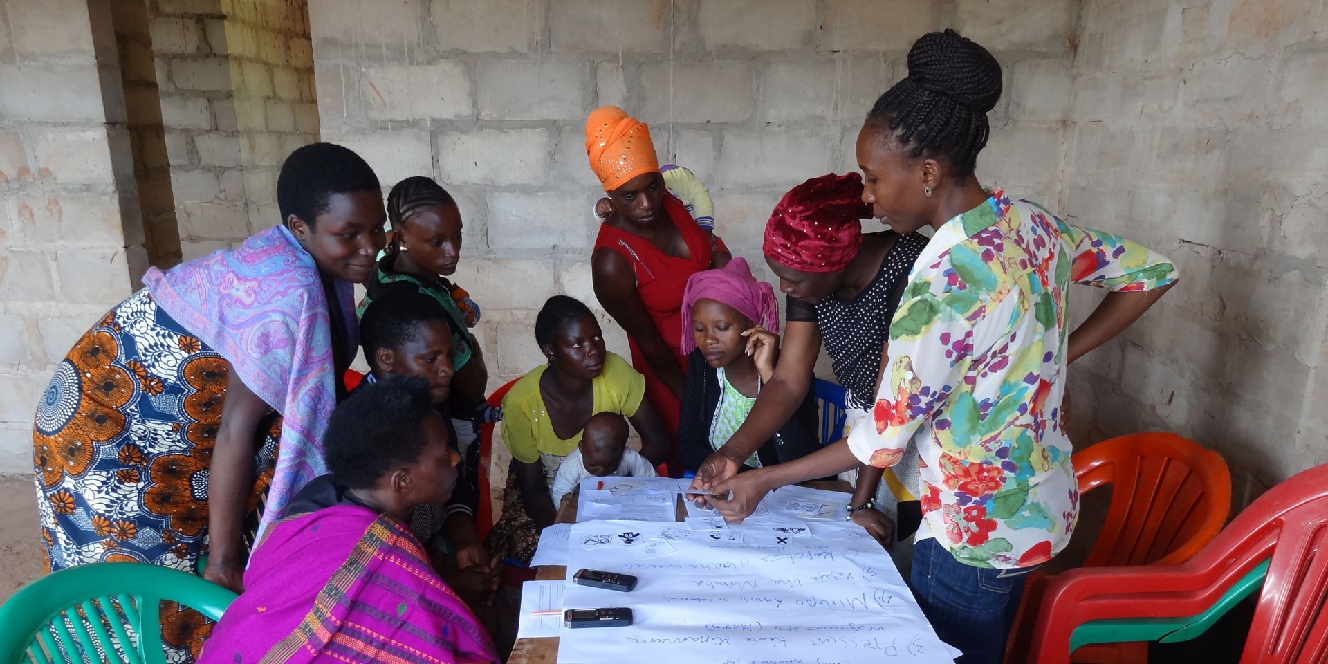 A group of women work at a table in Tanzania. Papers are laid out on it.