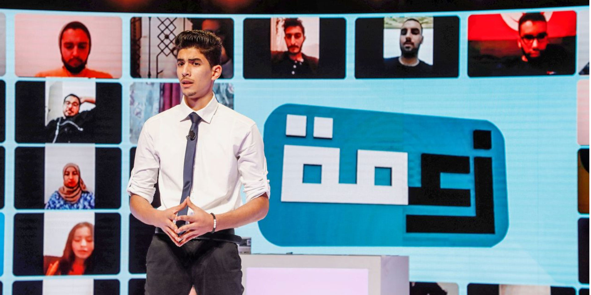 A young journalist stands in front of a giant screen and presents the news.