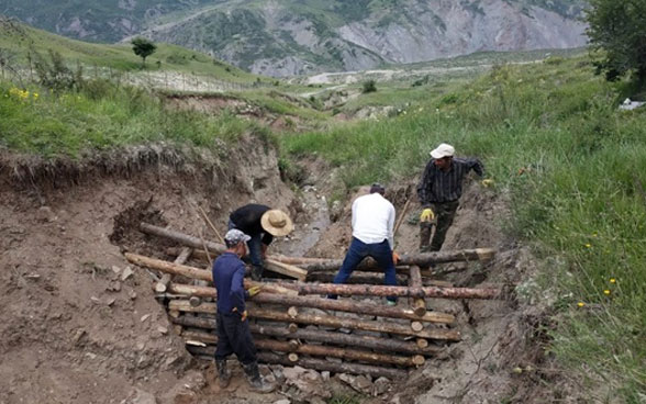Cuatro hombres construyen una presa de madera sencilla pero resistente en la ladera de una montaña.