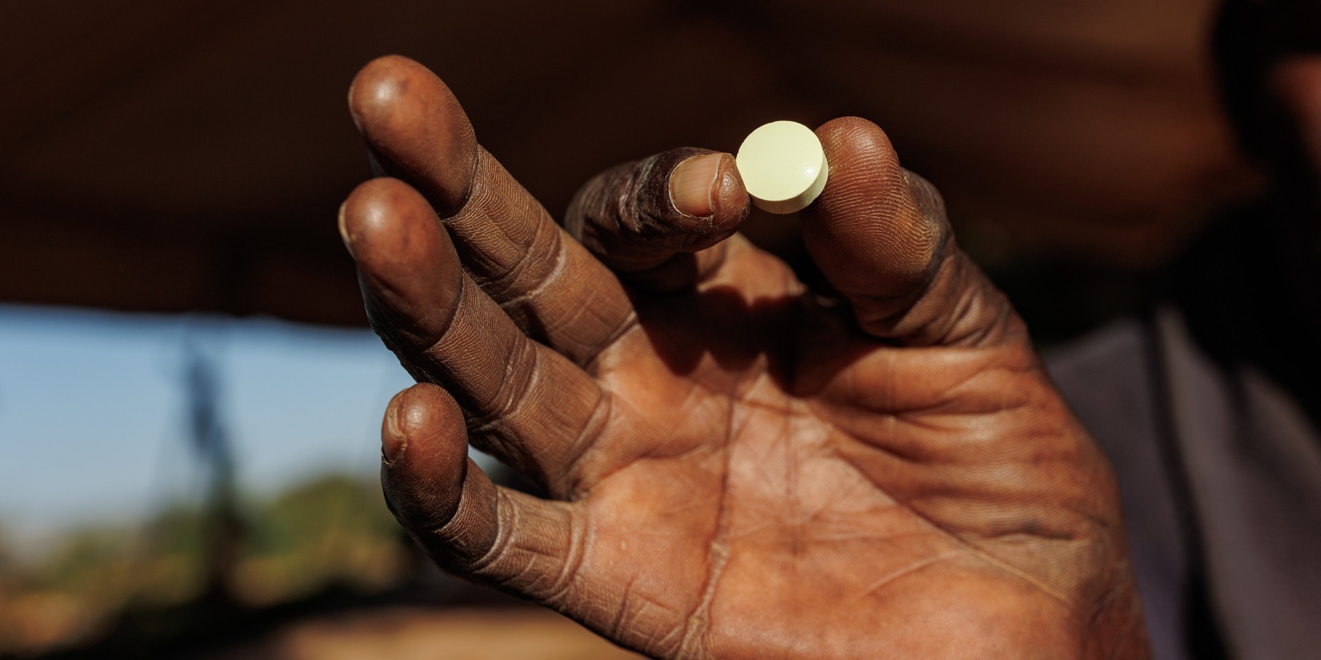 A hand holds a life-saving white pill between index finger and thumb.