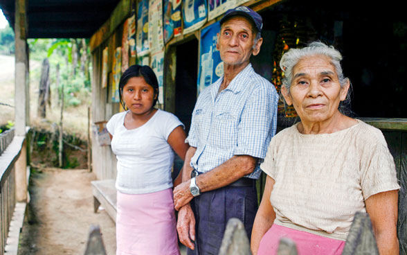Una pareja de ancianos posa con su nieta en la puerta de su negocio.