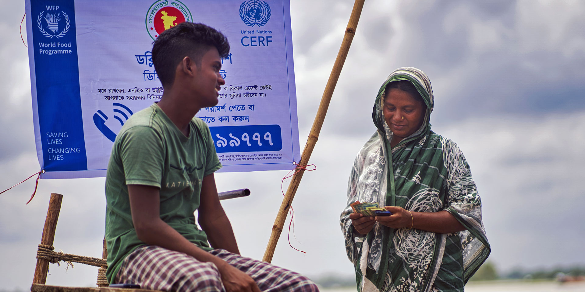 Una mujer a orillas de un río en Bangladesh cuenta junto a su hijo la ayuda en efectivo que recibió a través de un programa de acción anticipatoria.