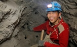 A man wearing a red pullover with a headlamp is sitting inside the mine 