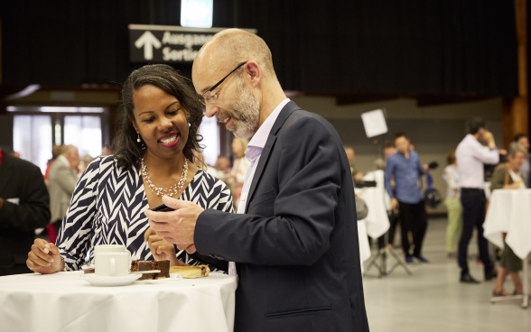 Two participants by a standing table, drinking coffee and having an animated discussion.