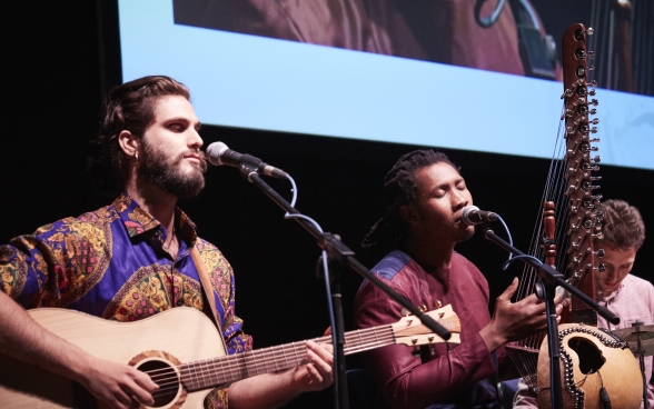 Les trois musiciens sont assis avec leurs instruments sur la scène devant leurs microphones.