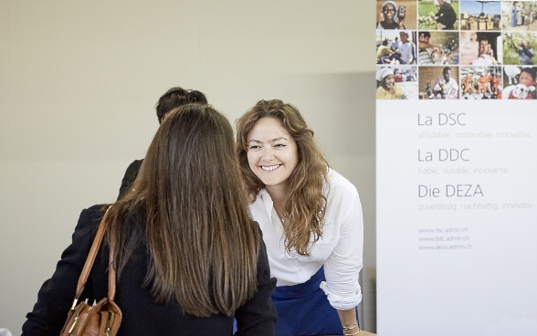 Une participante s’entretient avec une responsable du stand DDC/SECO. En arrière-plan l’on voit une affiche de la DDC.