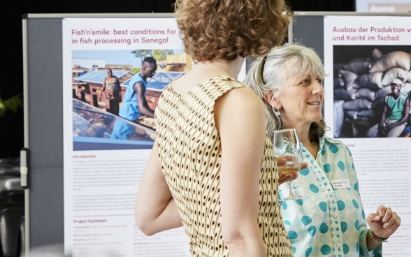 Deux participantes s’entretiennent debout devant un poster de l’exposition des organisations partenaires.