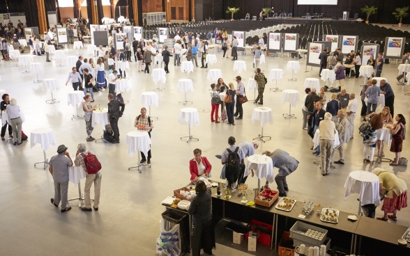 La Festhalle della Bernexpo dall’alto: i partecipanti si trattengono intorno a vari tavolini alti, parlano tra di loro, bevono o mangiano qualcosa.