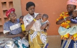 The photo shows three women each holding a baby. Two women feeding their babies. 