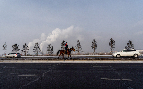 A horse with rider trotting along a main road. 