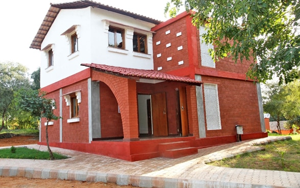 A red house surrounded by green trees, built from sustainable cement.