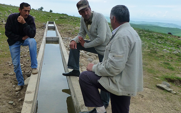 Three men speaking next to a trough.