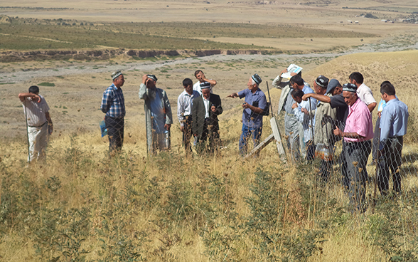 Tajik farmers standing in a field discussing the principle of crop rotation.