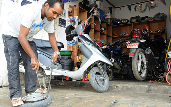 Un giovane uomo cambia il pneumatico della ruota di una Vespa.