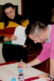 Three women look on as a young man writes something on a piece of paper.