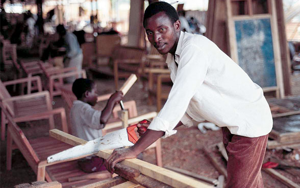 Un jeune homme scie une planche de bois.