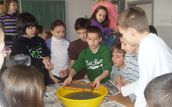 Boys and girls watching a fellow pupil doing an experiment with water.