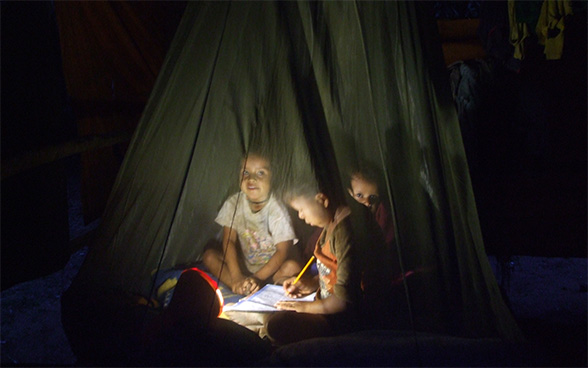 Tre bambini seduti per terra studiano.