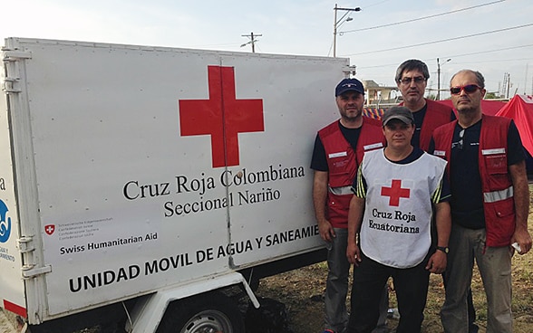 Drei Mitglieder des Schweizerischen Korps für humanitäre Hilfe und ein Mitarbeiter des ecuadorianischen Roten Kreuzes vor einem Anhänger mit Trinkwasser. 