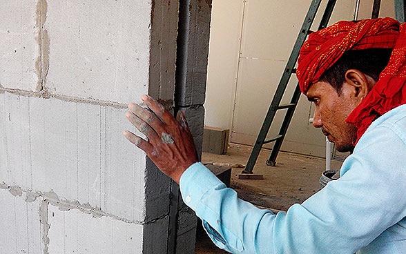 Ein indischer Arbeiter baut mit LC3-Zementblöcken eine Mauer.