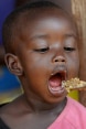 Une petite fille africaine ouvre grand la bouche pour avaler le contenu d’une cuillère tendue par sa maman à l’occasion du repas.
