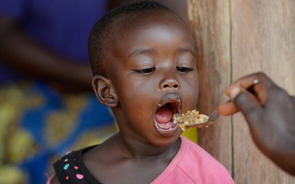 A young African girl opens wide for a spoonful of food from her mother