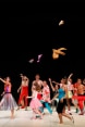 Dancers on a stage in colorful dresses throw clothes in the air.