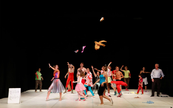 Dancers on a stage in colorful dresses throw clothes in the air.