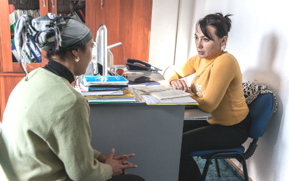 A lawyer sits at her desk and discusses with a woman.