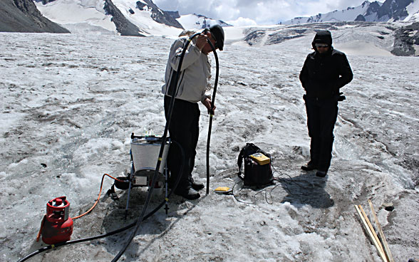 Two men working with specialist equipment on a glacier. 