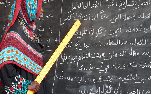 Während eines Kurses in einem Alphabetisierungszentrum in Oum Hadjer, Region Batha, Tschad, liest eine junge Mutter mit einem Lineal in der Hand an der Wandtafel. 