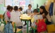 Une photo de l’intérieur d’une classe avec une enseignante qui se tient devant un groupe d’enfants en leur montrant un livre. 