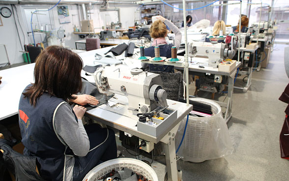 In a large room, five women sit one behind the other at sewing machines and sew.