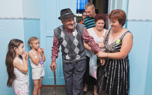 A laughing elderly gentleman is escorted out of a room by two women.