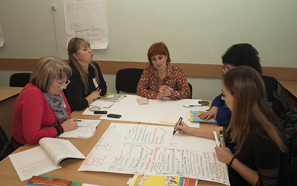 Plusieurs femmes en discussion autour d’une table couverte de notes et de brochures.