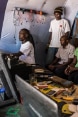 a man repairing a computer in his workshop, watched by six visitors.