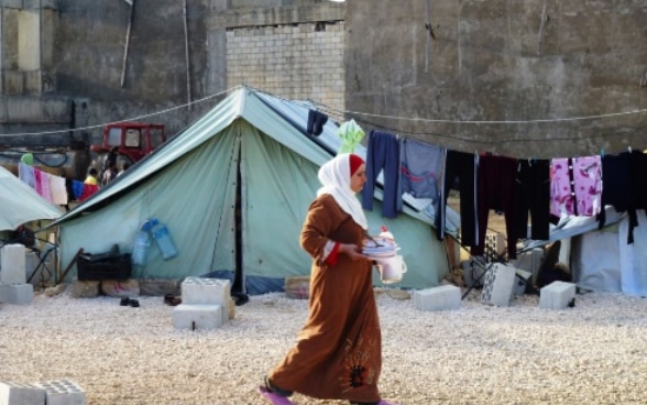 Une femme marche devant une tente de réfugiés.