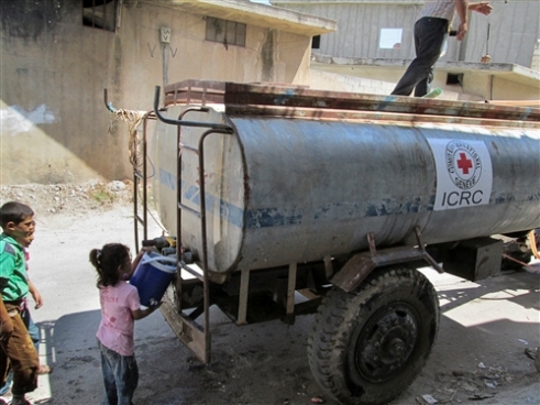 Ein kleines Mädchen, das zu den intern Vertriebenen zählt, holt Wasser bei einem Wassertankwagen des IKRK in der Ortschaft Talbiseh, am Rand von Homs.