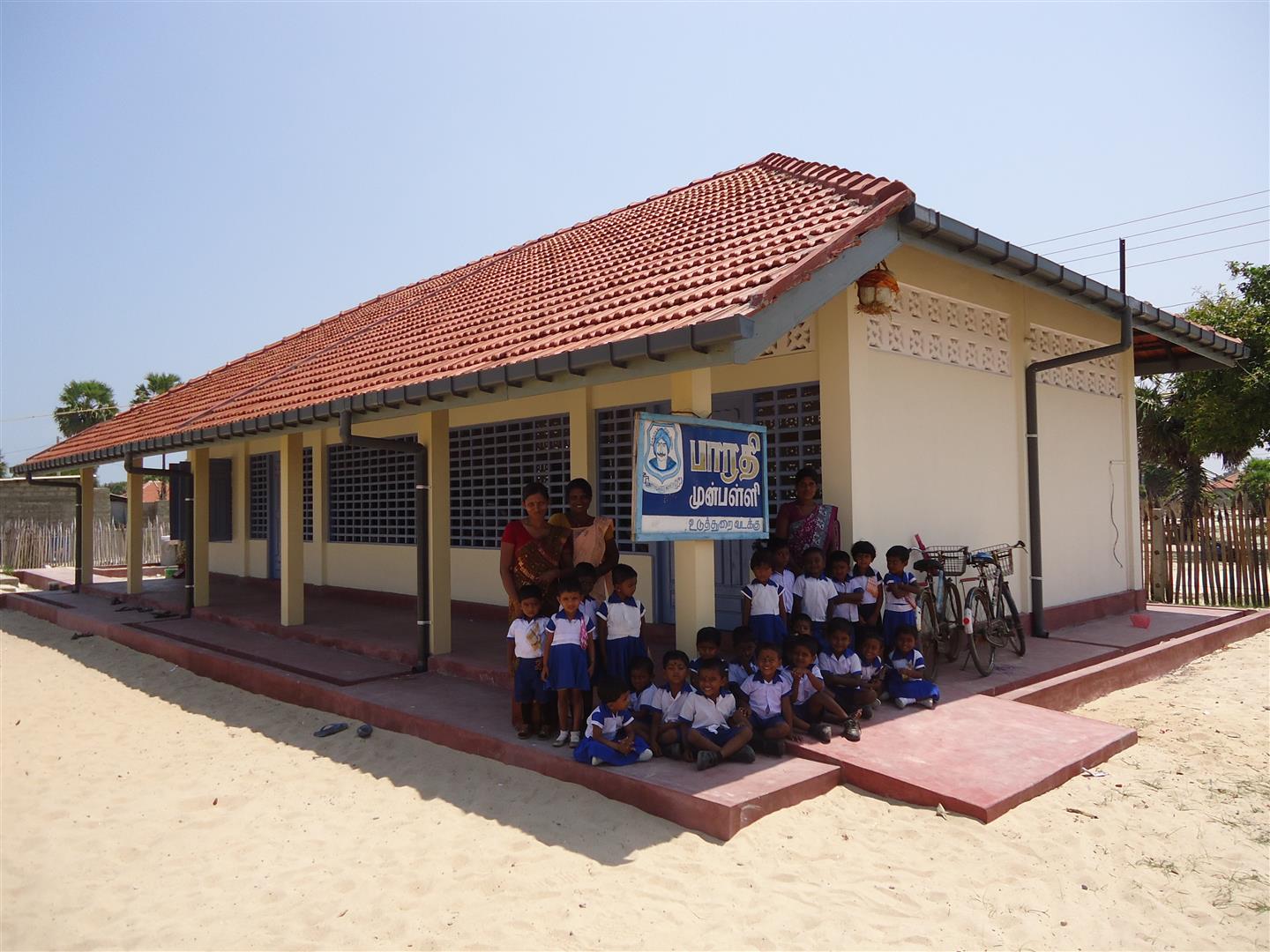 Un gruppo di bambini posano con la loro maestra davanti alla scuola rinnovata.