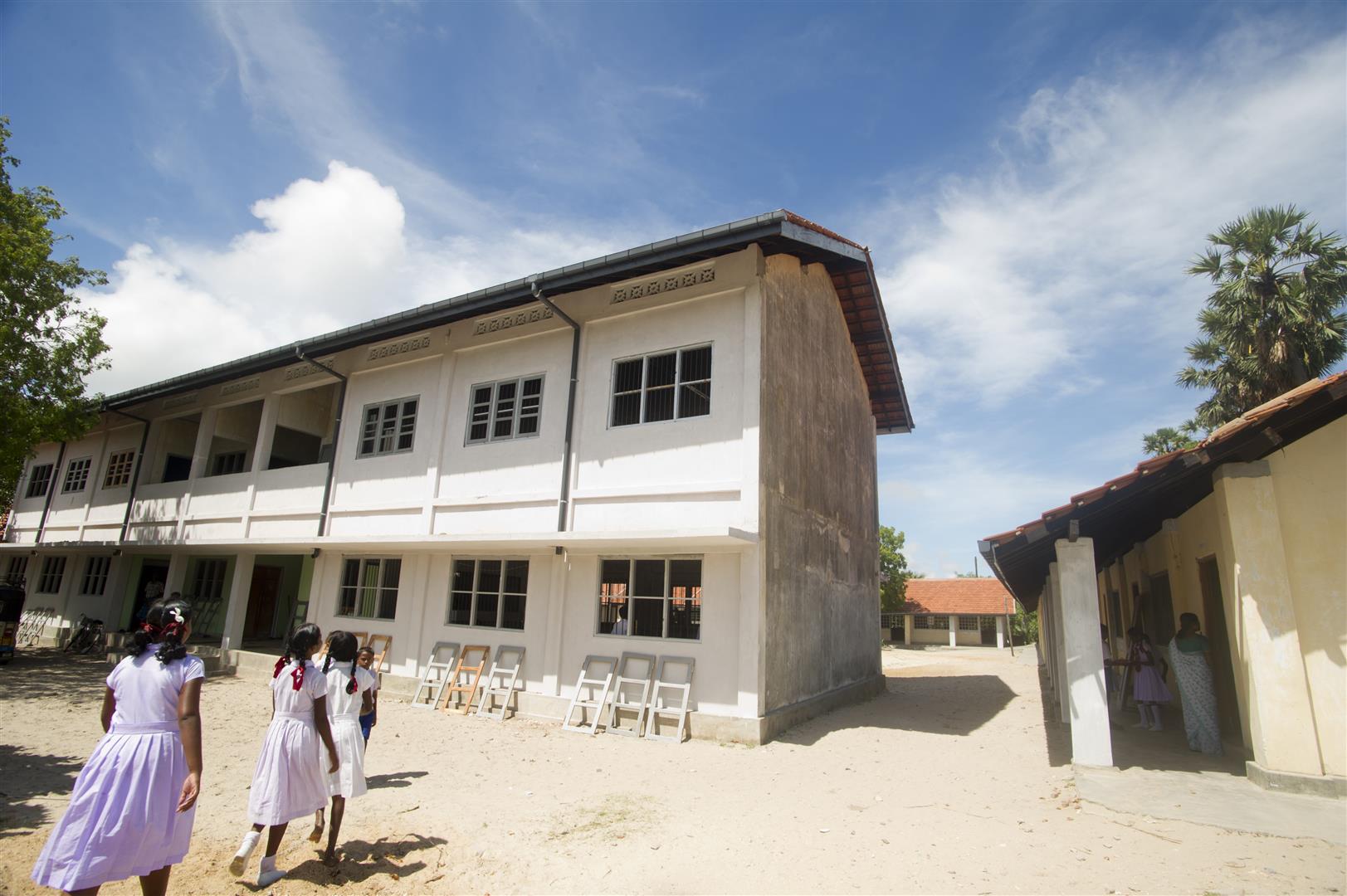 Tre scolare camminano verso la loro scuola, costruita su due piani.