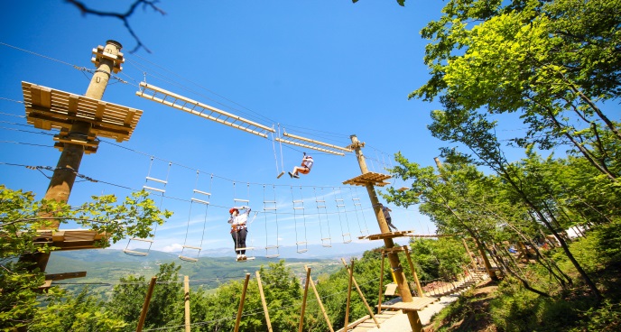 Due persone camminano su delle corde in un parco avventura.