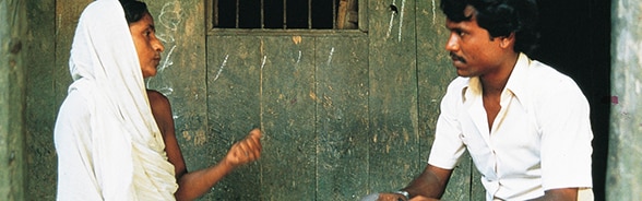 Une femme et un homme discutent devant une cabane.