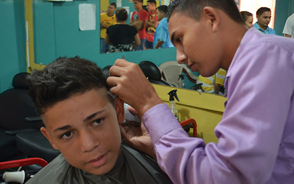 Un apprendista parrucchiere taglia i capelli a un ragazzo